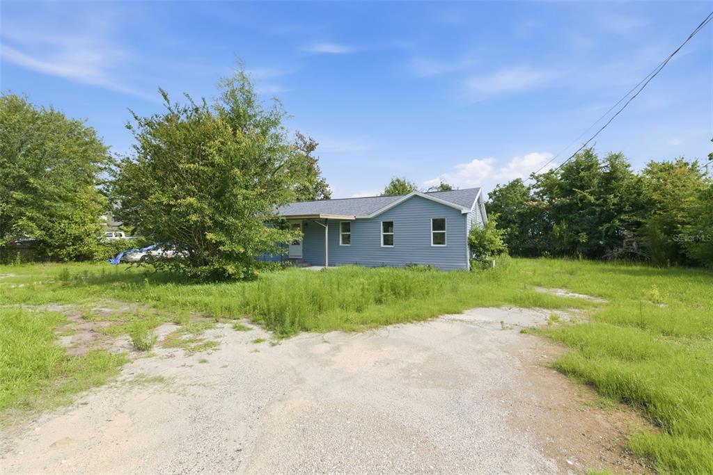 A blue, single-story house with a gravel driveway sits on a grassy, overgrown lot — 5205 E 11TH STREET, PANAMA CITY, FL
