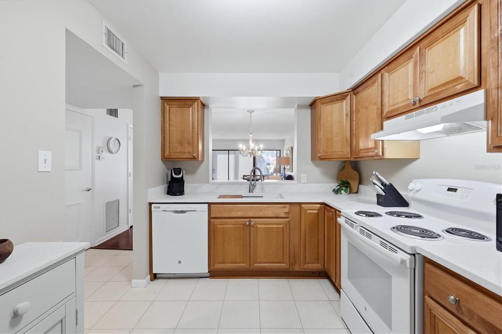 A kitchen features wood cabinets, white appliances, a tiled floor, and a pass-through window — 5216 LAKE VILLAGE DRIVE UNIT 71, SARASOTA, FL