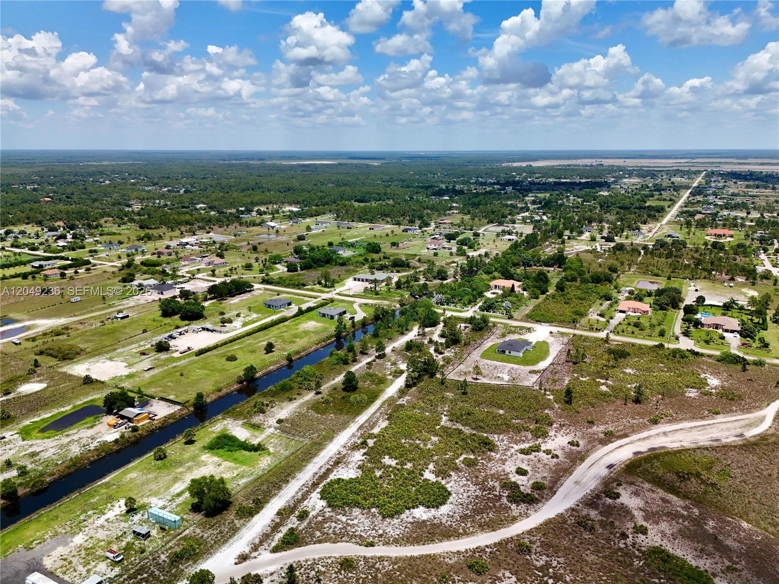An aerial view shows a rural landscape with scattered houses, a canal, and dirt roads — 0 60th Ave NE, Naples FL 34120, NAPLES, FL