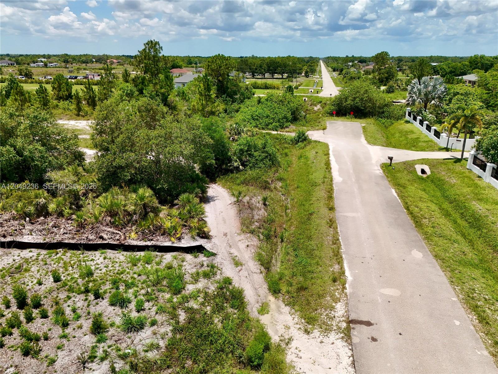 An aerial view shows a paved road leading toward a rural landscape with scattered trees — 0 60th Ave NE, Naples FL 34120, NAPLES, FL