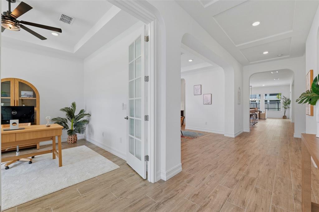 A home office with French doors opens into a hallway with wood-look tile flooring — 6015 MARSH TRAIL DRIVE, ODESSA, FL