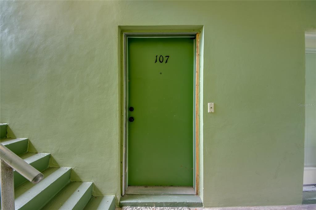 A green exterior door numbered 107 is positioned next to a set of concrete stairs — 2544 1ST STREET UNIT 107, FORT MYERS, FL