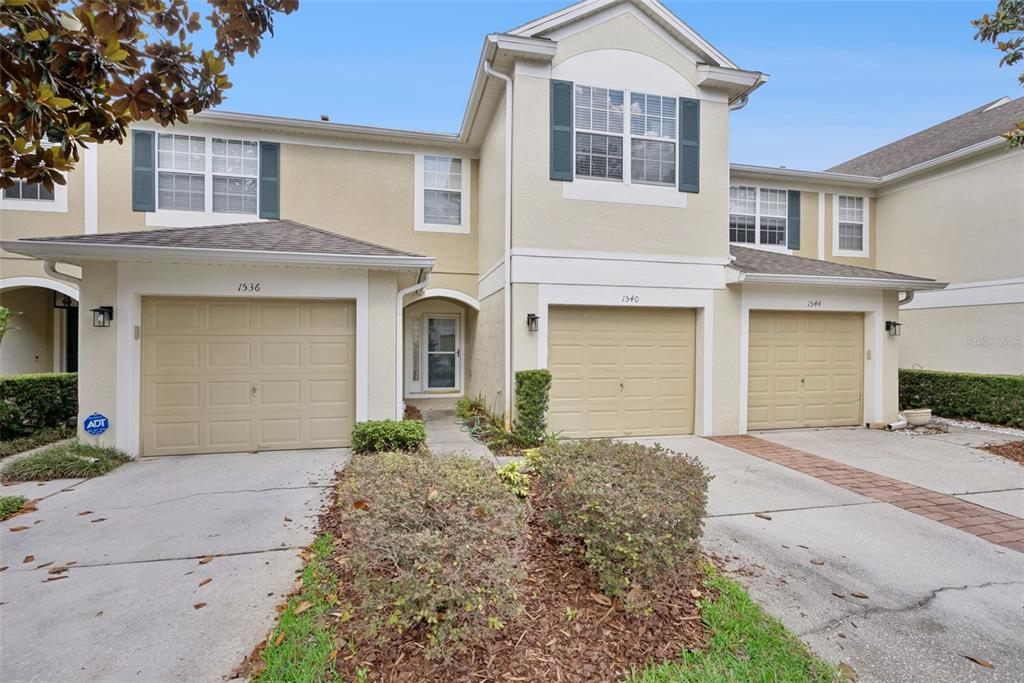 A three-unit townhouse exterior with beige stucco walls, tan garage doors, and dark shutters — 1540 FLORENTINO LANE, WINTER PARK, FL