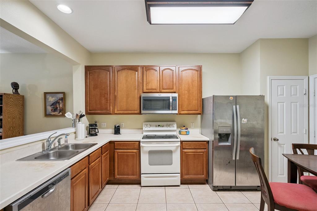 A kitchen features wood cabinets, white appliances, a stainless steel refrigerator, and tile flooring — 1540 FLORENTINO LANE, WINTER PARK, FL