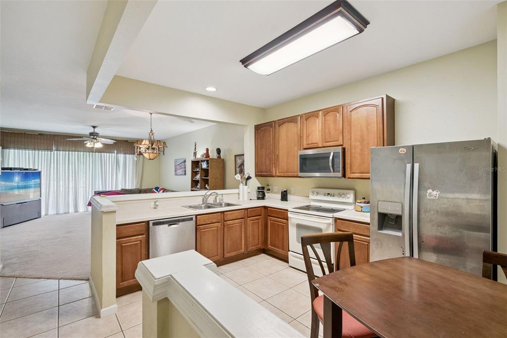 A kitchen with wood cabinets, stainless steel appliances, and tile flooring overlooks a living area — 1540 FLORENTINO LANE, WINTER PARK, FL