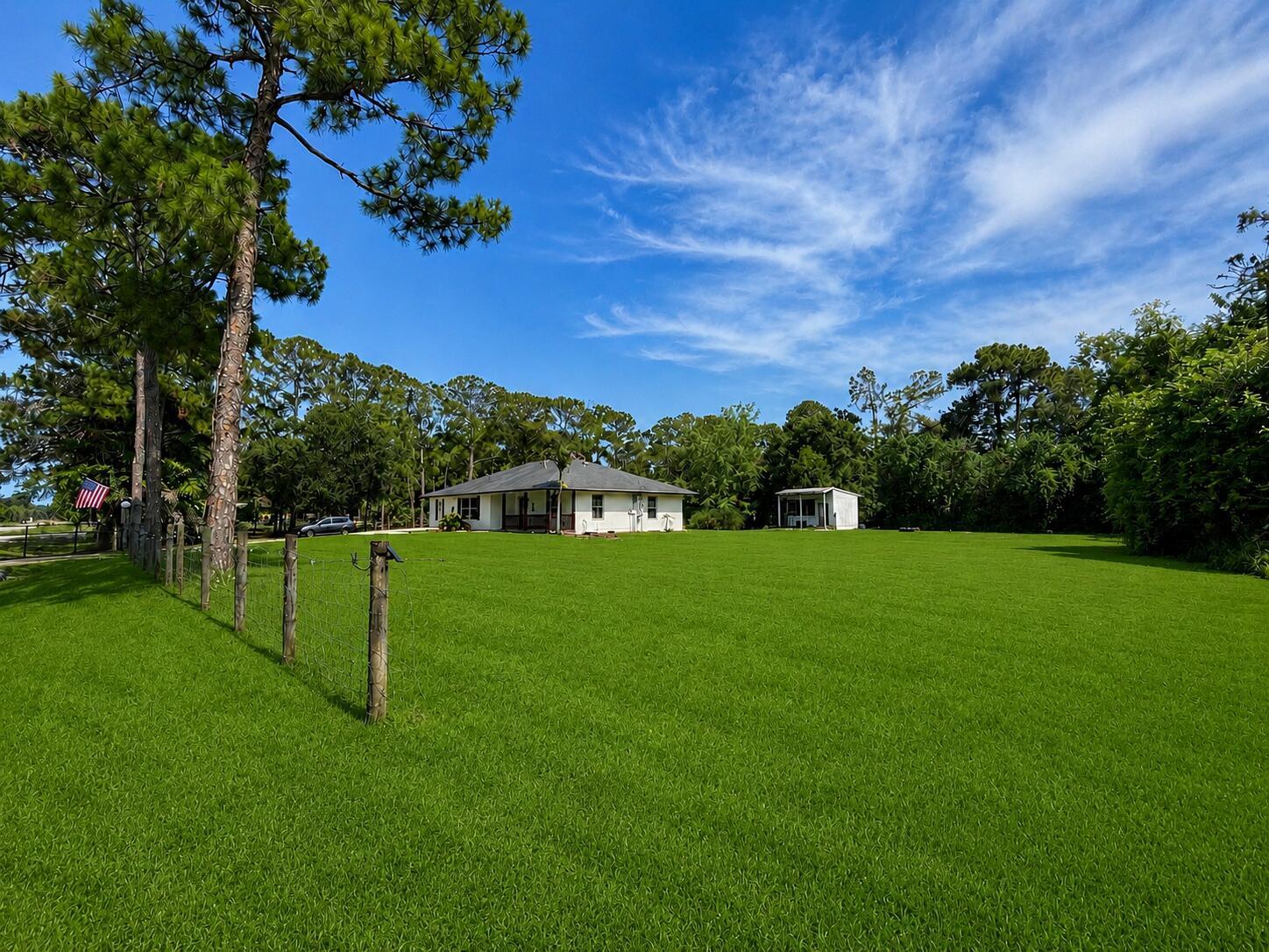 A white house sits on a large, grassy lot bordered by a wire fence — 14732 66th Street N, Loxahatchee FL 33470, LOXAHATCHEE, FL