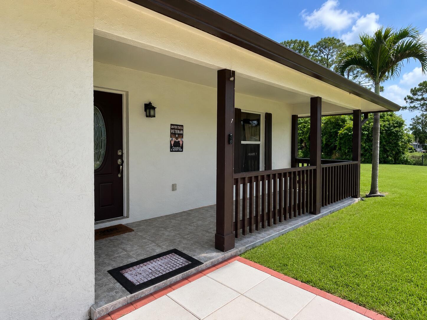 A covered front porch with a dark wooden railing, tiled flooring, and a brown front door — 14732 66th Street N, Loxahatchee FL 33470, LOXAHATCHEE, FL