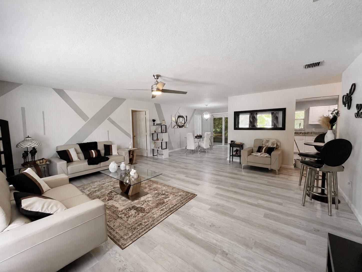 A spacious living room features light wood-look flooring, a geometric accent wall, and neutral furniture — 14732 66th Street N, Loxahatchee FL 33470, LOXAHATCHEE, FL