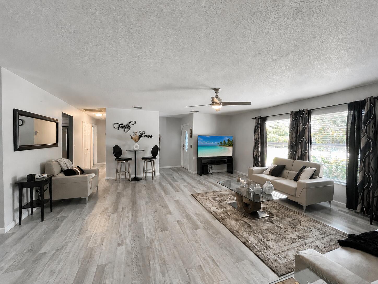 A spacious living room features light wood-look flooring, a ceiling fan, and neutral-toned furniture — 14732 66th Street N, Loxahatchee FL 33470, LOXAHATCHEE, FL