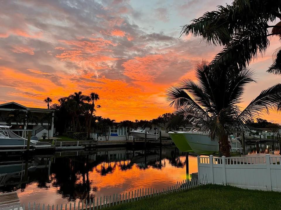 A vibrant sunset glows over a canal with docked boats and palm trees — 4052 14TH WAY NE, ST PETERSBURG, FL