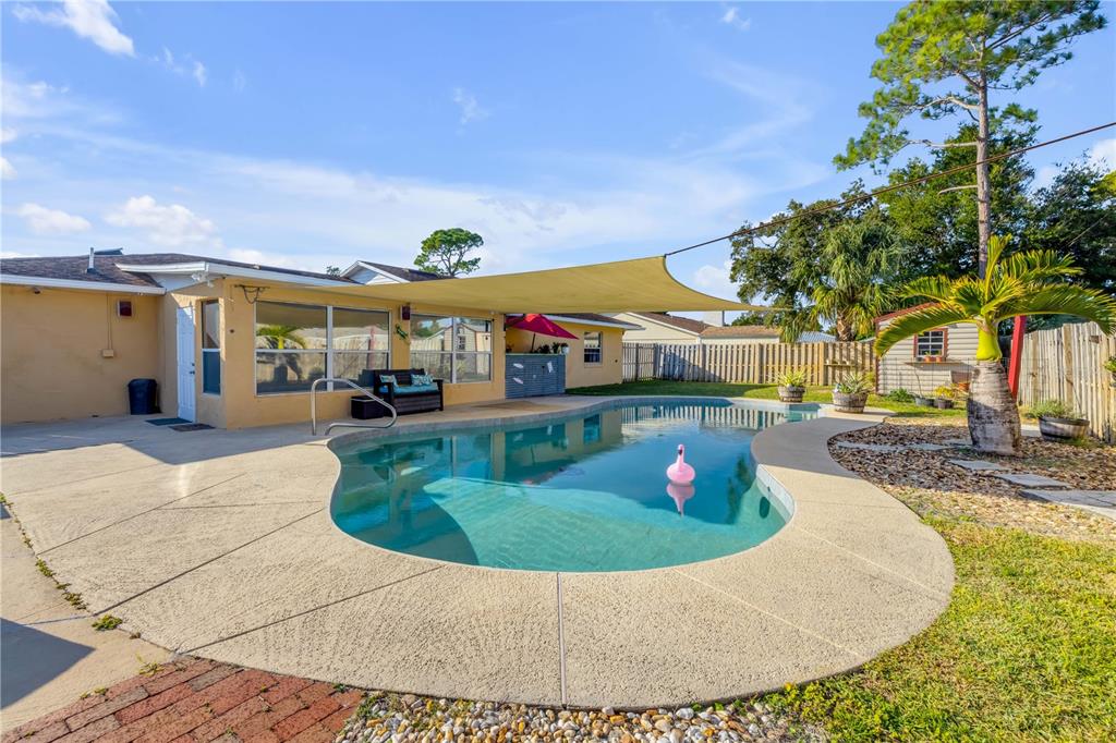 A backyard features a swimming pool, a tan shade sail, and a concrete patio area — 2425 TRAVELERS PALM DRIVE, EDGEWATER, FL