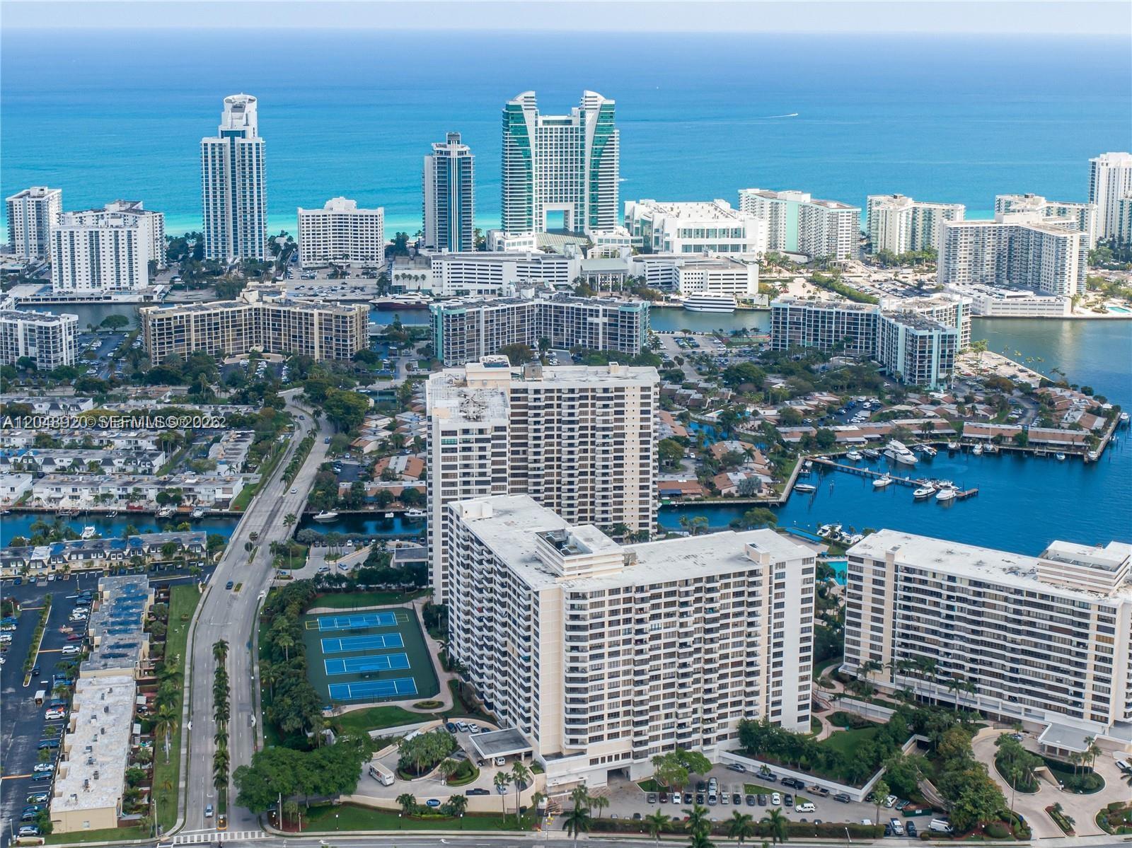 An aerial view shows high-rise residential buildings, a tennis court, and a marina in Florida — 600 Three Islands Blvd # 1113, Hallandale Beach FL 33009, HALLANDALE BEACH, FL