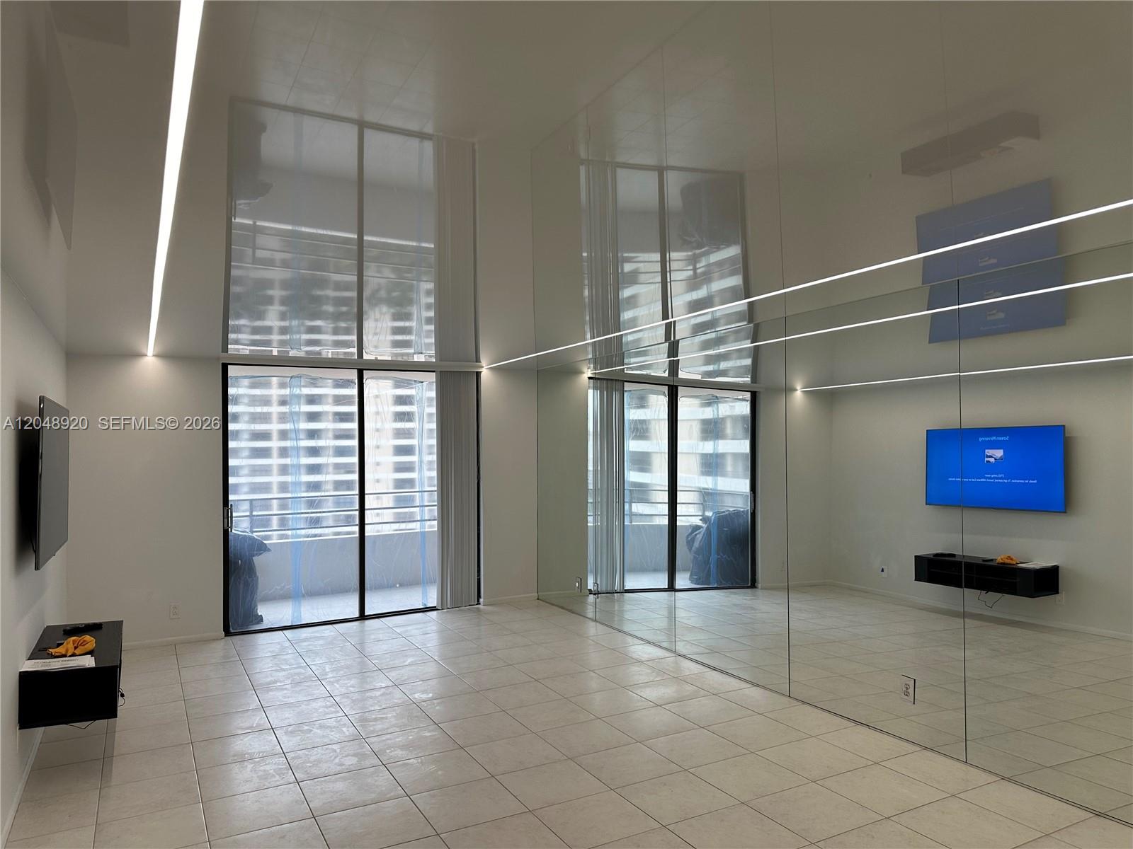 A minimalist room features white tile floors, a mirrored wall, and a sliding glass door — 600 Three Islands Blvd # 1113, Hallandale Beach FL 33009, HALLANDALE BEACH, FL