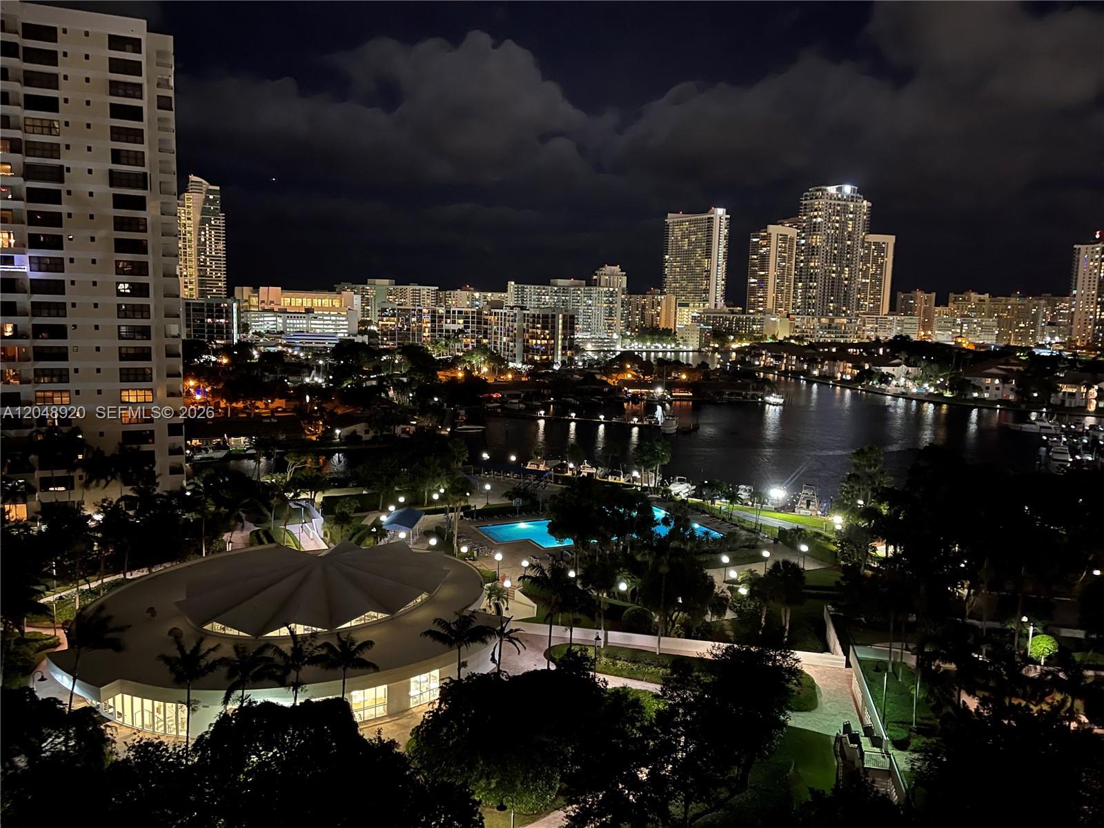 An elevated night view of a waterfront residential complex with a pool and city skyline — 600 Three Islands Blvd # 1113, Hallandale Beach FL 33009, HALLANDALE BEACH, FL
