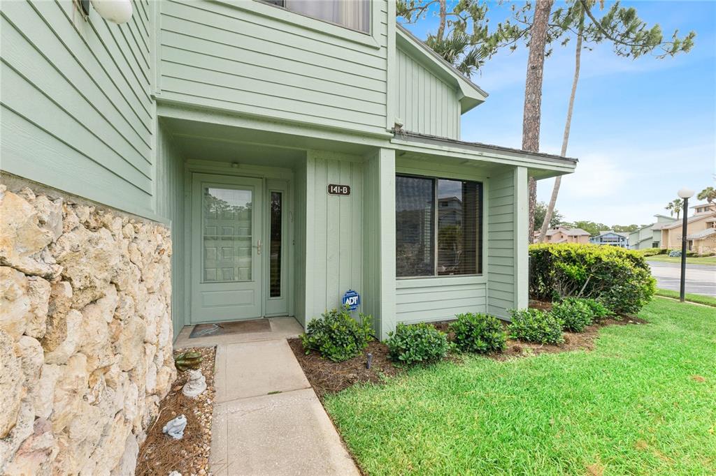 A green-sided residential building entrance features a stone facade, a front door, and landscaping — 141 GOLDEN EYE DRIVE UNIT B, DAYTONA BEACH, FL