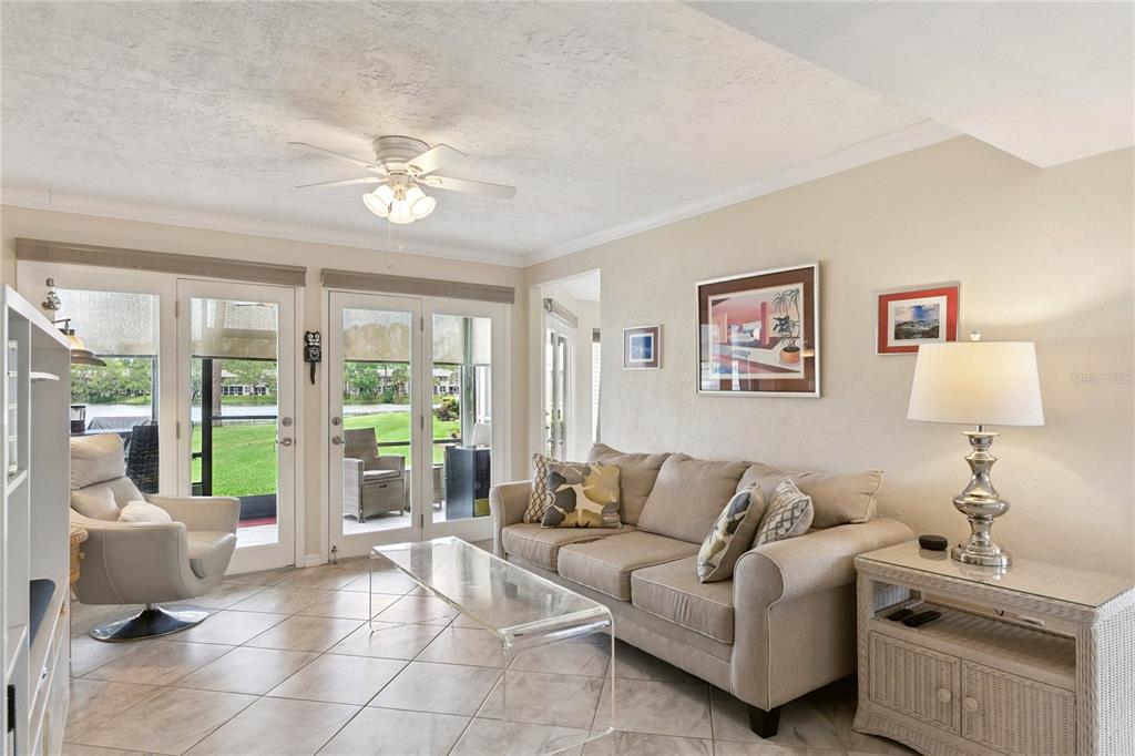 A living room with tile floors, a beige sofa, and glass doors overlooking a lake — 141 GOLDEN EYE DRIVE UNIT B, DAYTONA BEACH, FL
