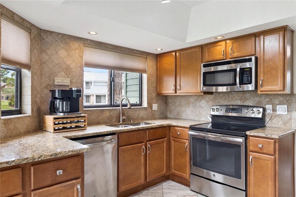 A kitchen with wood cabinets, granite countertops, stainless steel appliances, and a tiled backsplash — 141 GOLDEN EYE DRIVE UNIT B, DAYTONA BEACH, FL