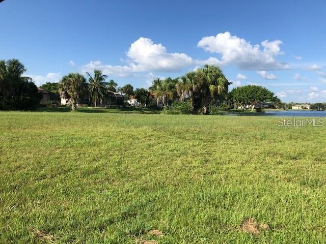 A grassy vacant lot overlooks a pond with palm trees and houses in the background — 17209 BARCREST LANE, PUNTA GORDA, FL