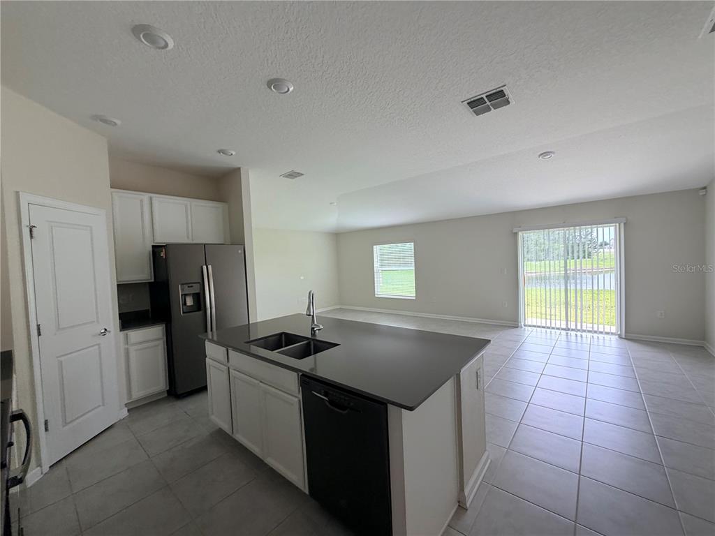 A kitchen with white cabinets, a dark island, and tile flooring opens to a living area — 16419 GLASSY LOCH LOOP, CLERMONT, FL