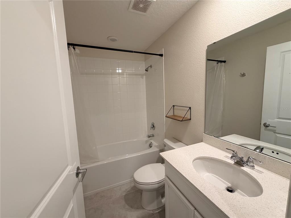 A bathroom features a white vanity, a toilet, and a shower-tub combination with white tiles — 16419 GLASSY LOCH LOOP, CLERMONT, FL