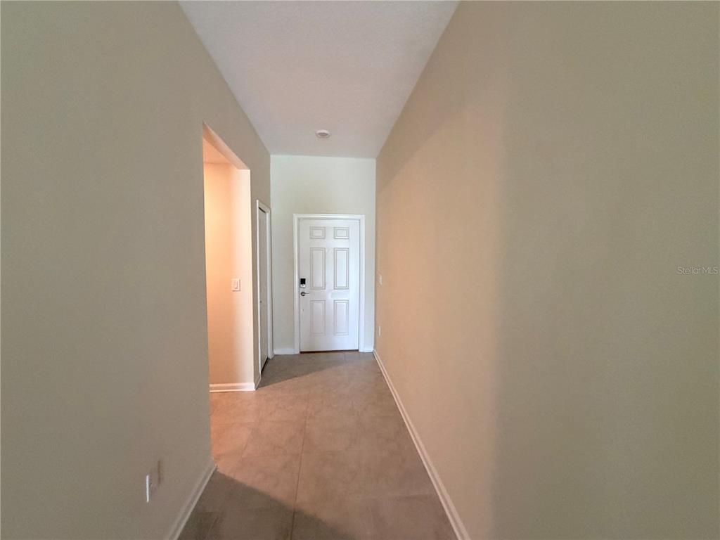A hallway with beige walls and tile flooring leads to a white front door — 16419 GLASSY LOCH LOOP, CLERMONT, FL