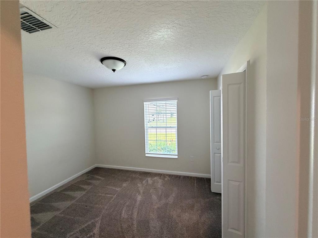 A bedroom with beige walls, brown carpet, a ceiling light, and a window with blinds — 16419 GLASSY LOCH LOOP, CLERMONT, FL