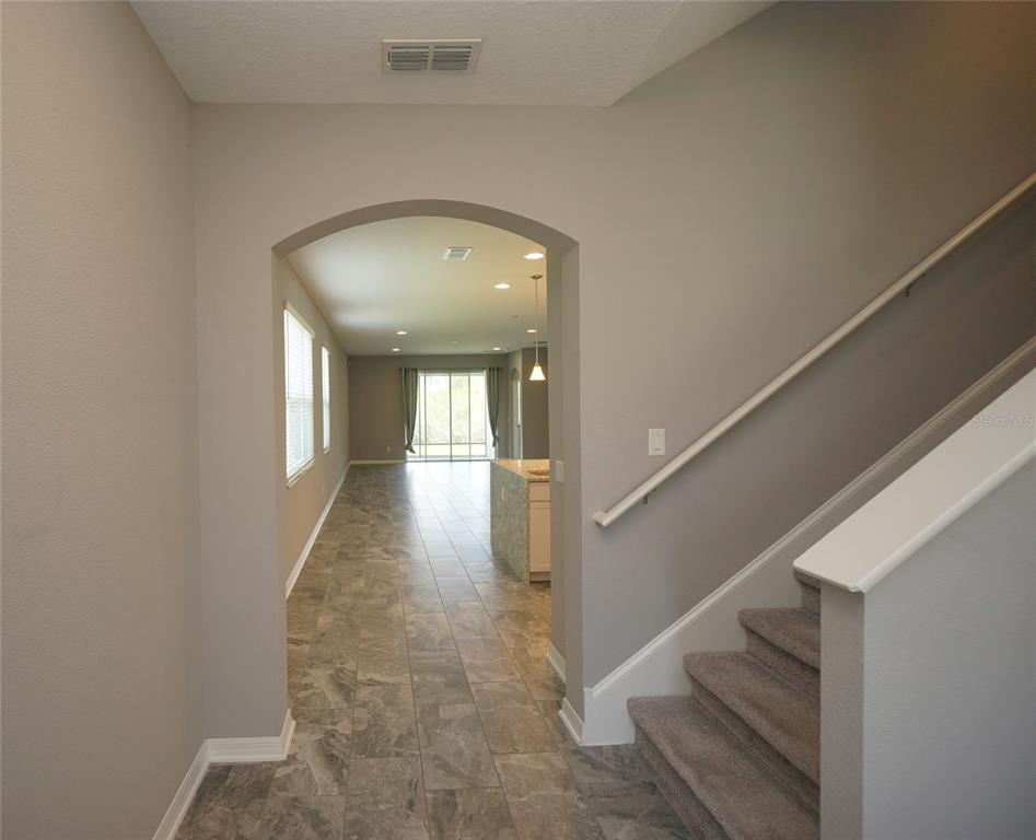 An entryway with tile flooring leads to an open-concept kitchen and living area with stairs — 19460 BLOSSOM VINE LANE, LUTZ, FL