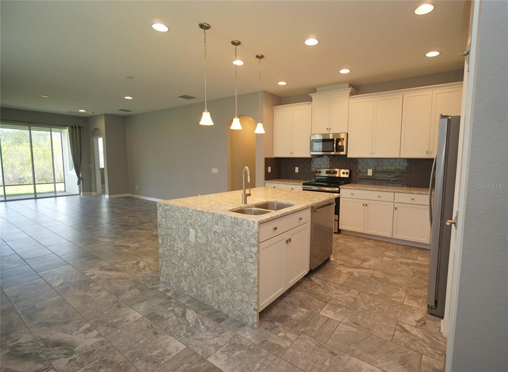 A kitchen with white cabinets, granite countertops, and an island overlooks an open living area — 19460 BLOSSOM VINE LANE, LUTZ, FL