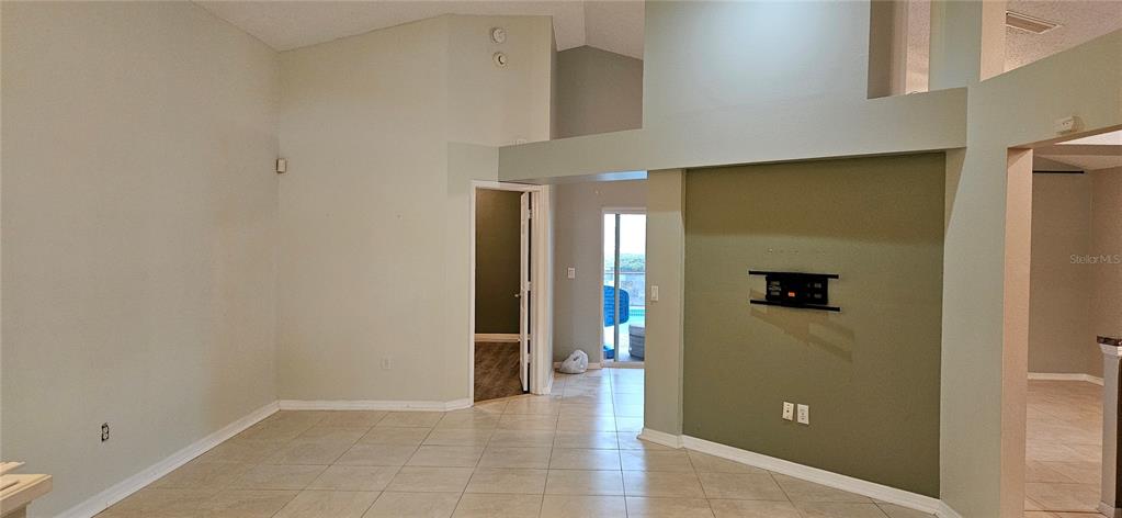 An interior view of a living area with tile flooring, vaulted ceilings, and an accent wall — 3186 BENTLEY DRIVE, PALM HARBOR, FL