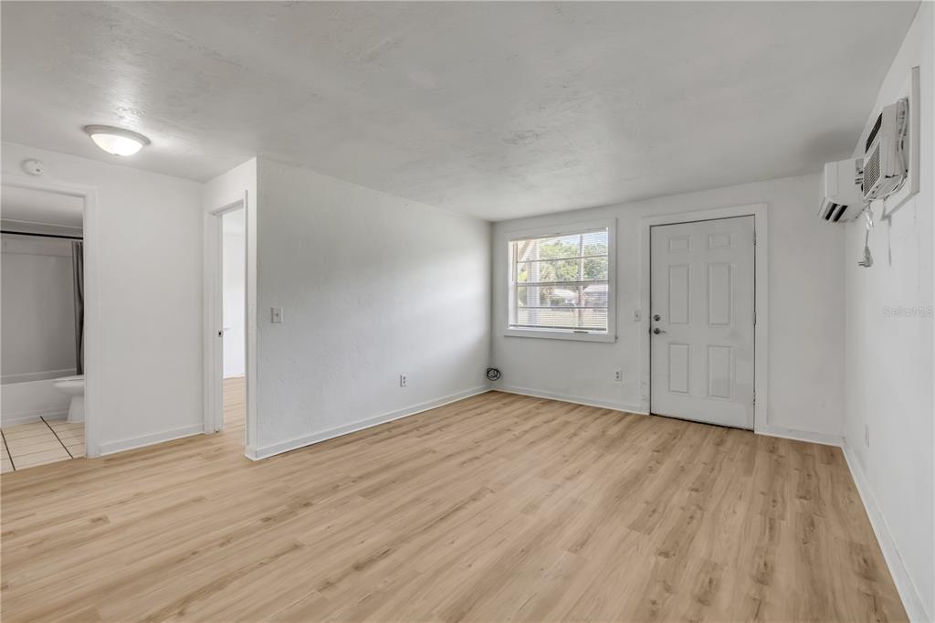 An empty room with light wood-look flooring, white walls, a window, and an exterior door — 1051 JUNE TERRACE, DAYTONA BEACH, FL