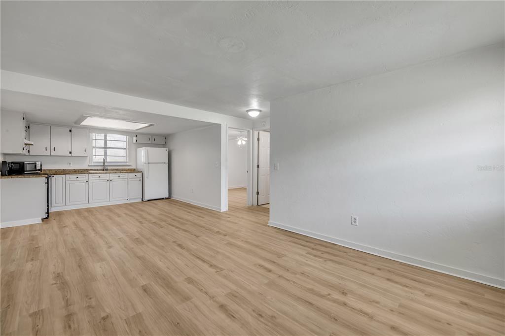 An open-concept kitchen and living area features white cabinets, light wood flooring, and white walls — 1051 JUNE TERRACE, DAYTONA BEACH, FL