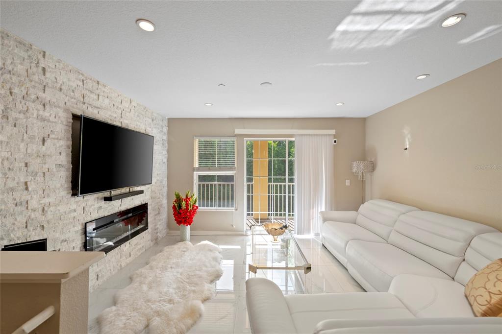 A living room features a stone accent wall, a fireplace, and a white leather sofa — 8825 WHITE SAGE LOOP, LAKEWOOD RANCH, FL