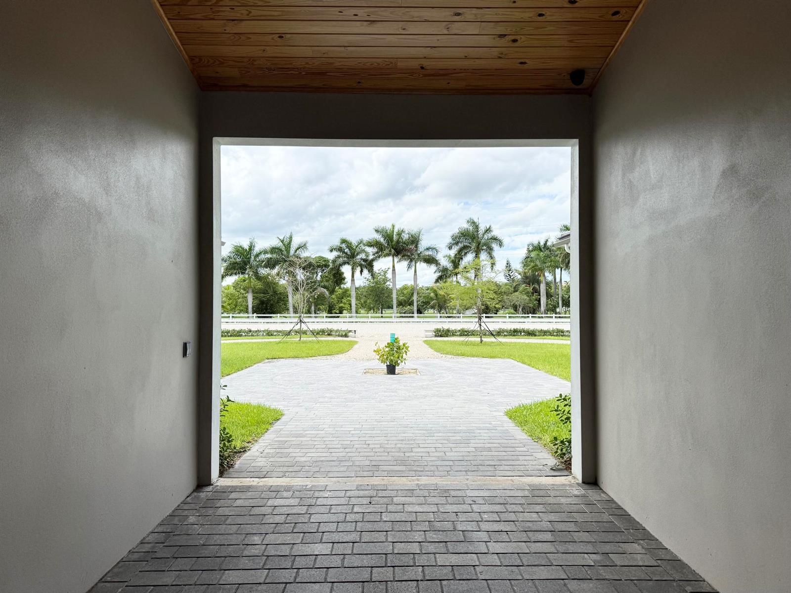 A view from a covered entryway looking out onto a paved courtyard and palm trees — 19550 Egret Lane, Loxahatchee FL 33470, LOXAHATCHEE, FL