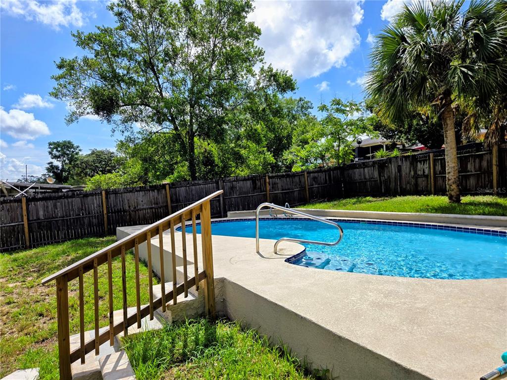 An outdoor swimming pool with a metal handrail sits next to a wooden staircase — 6070 ASHLAND DRIVE, SPRING HILL, FL