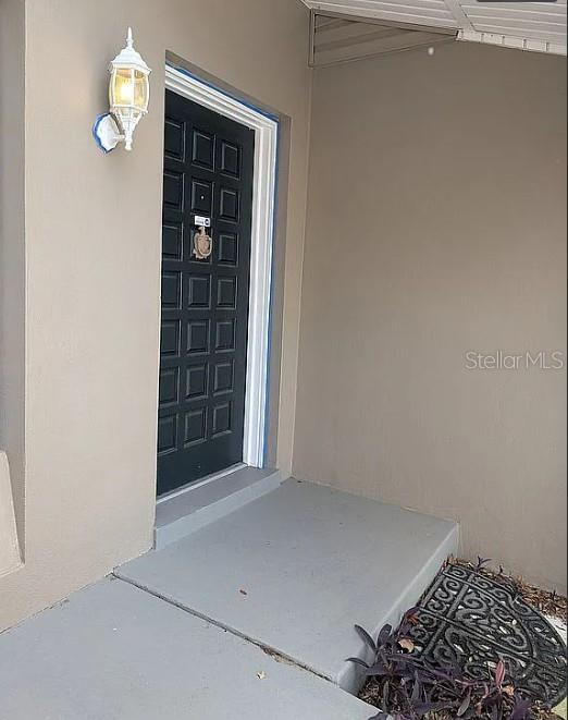 A black front door with a knocker is set into a beige exterior wall — 6070 ASHLAND DRIVE, SPRING HILL, FL