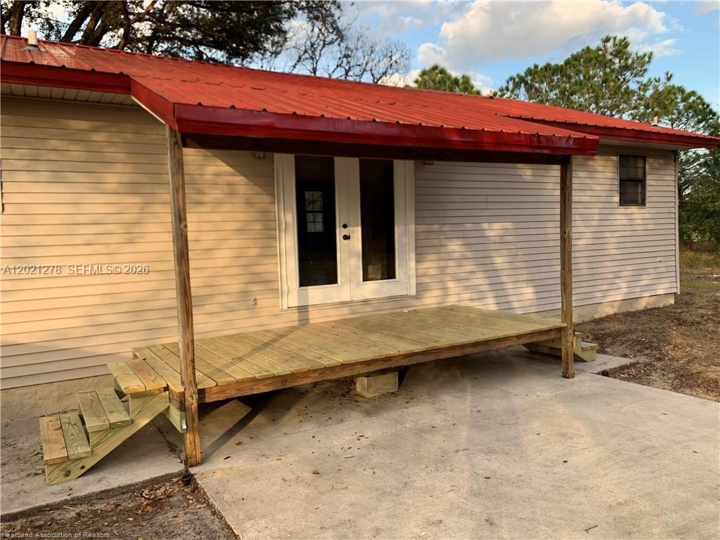 A wooden deck with stairs sits under a red metal roof attached to a house — 2225 N UNICORN # 0, Avon Park FL 33825, AVON PARK, FL