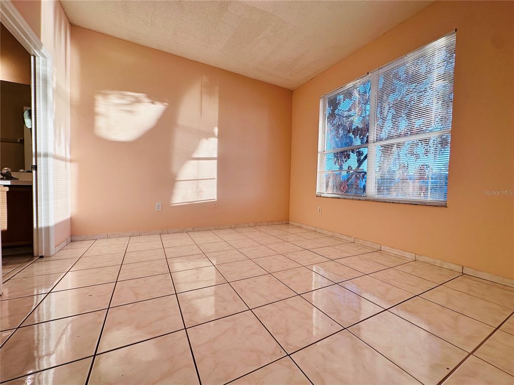 An empty room features peach-colored walls, light-colored tile flooring, and a large window with blinds — 13343 SUMMERTON DRIVE, ORLANDO, FL