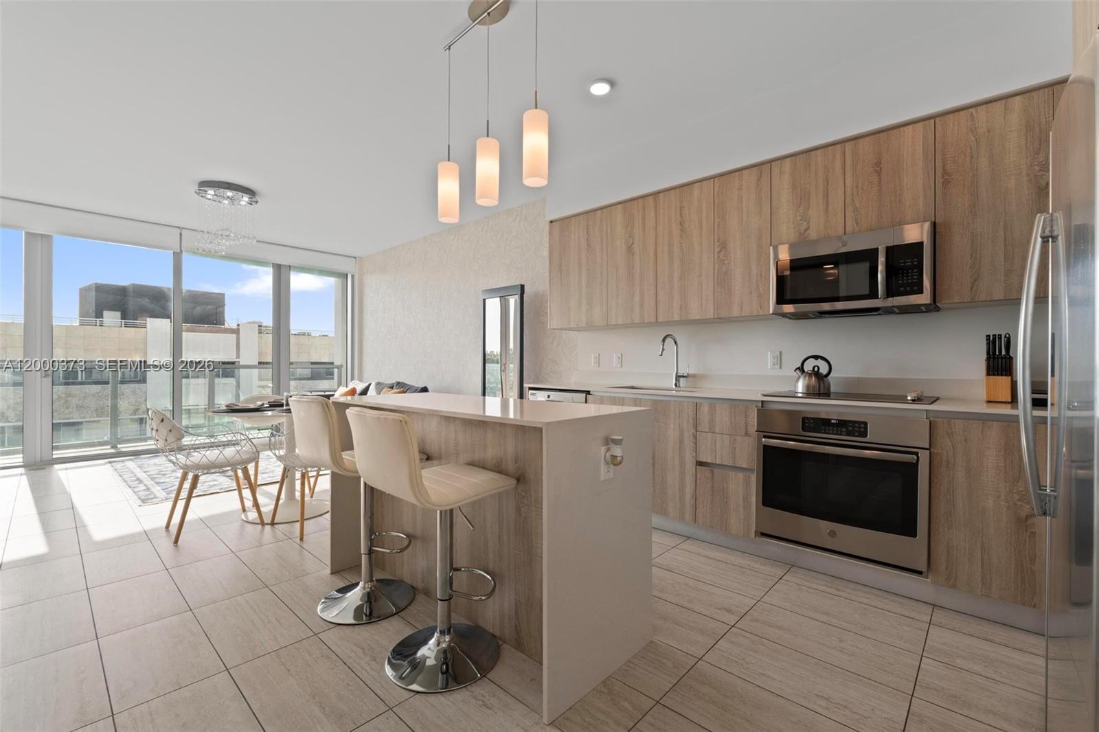 A modern kitchen features light wood cabinetry, stainless steel appliances, and a breakfast bar island — 3900 Biscayne Blvd # 418, Miami FL 33137, MIAMI, FL