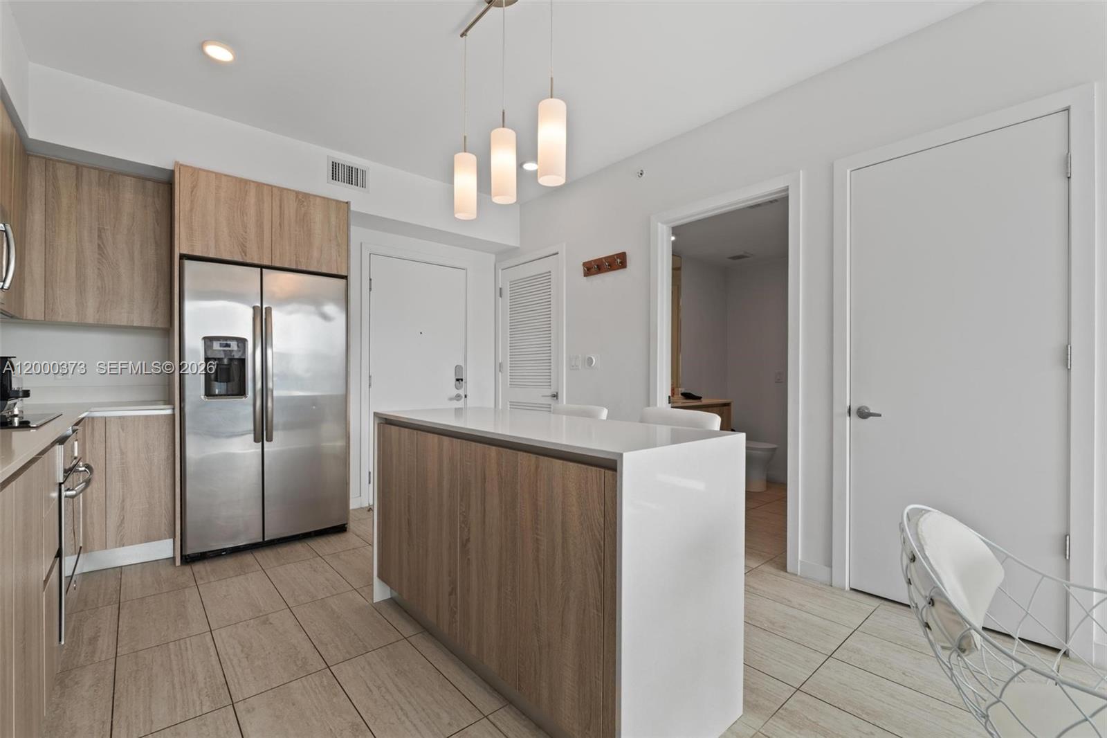 A modern kitchen features wood-toned cabinetry, stainless steel appliances, and a white waterfall island — 3900 Biscayne Blvd # 418, Miami FL 33137, MIAMI, FL