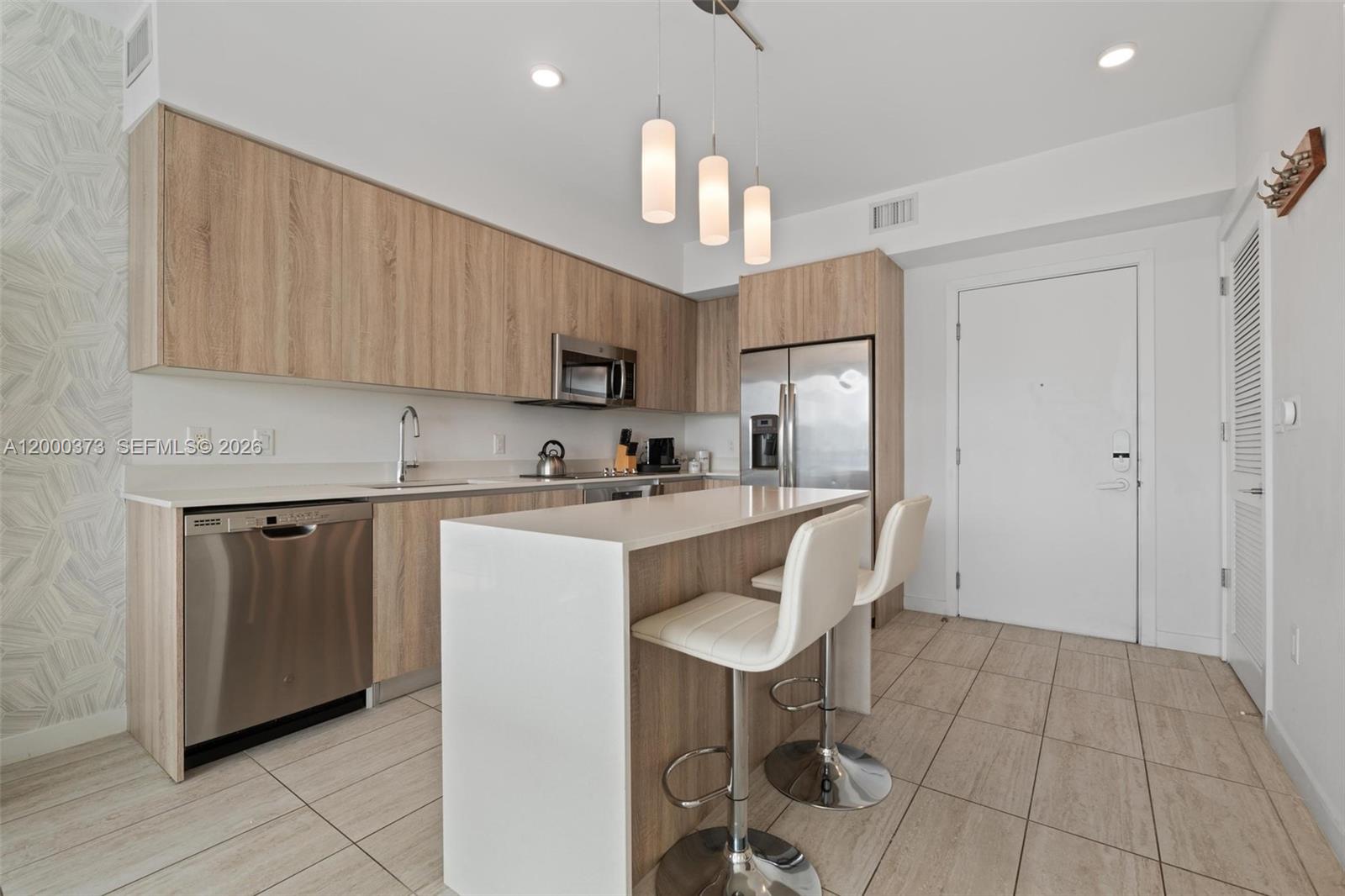 A modern kitchen features light wood cabinets, stainless steel appliances, and a white breakfast bar — 3900 Biscayne Blvd # 418, Miami FL 33137, MIAMI, FL