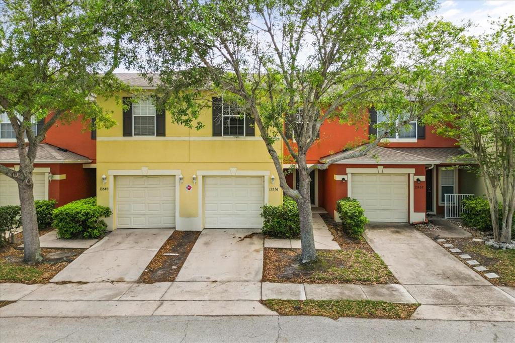 An exterior view of three attached townhomes with garages and orange and yellow stucco facades — 13536 TEA ROSE WAY UNIT 119, ORLANDO, FL