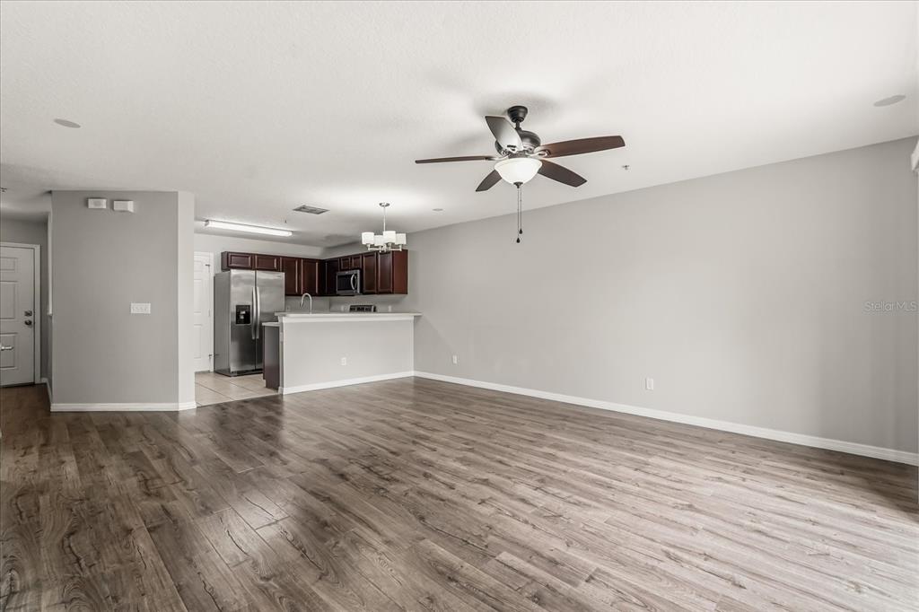 An open-concept living area with wood-look flooring, a ceiling fan, and an adjacent kitchen — 13536 TEA ROSE WAY UNIT 119, ORLANDO, FL