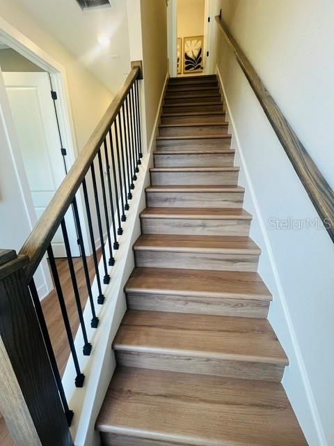 A staircase with wood-look steps and a black metal railing leads to an upper landing — 15501 HAMLIN PARK DRIVE, WINTER GARDEN, FL