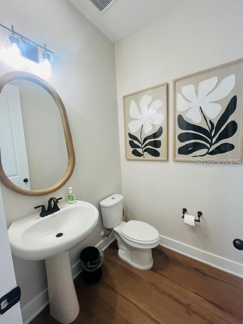 A powder room features a pedestal sink, a toilet, a round mirror, and floral wall art — 15501 HAMLIN PARK DRIVE, WINTER GARDEN, FL