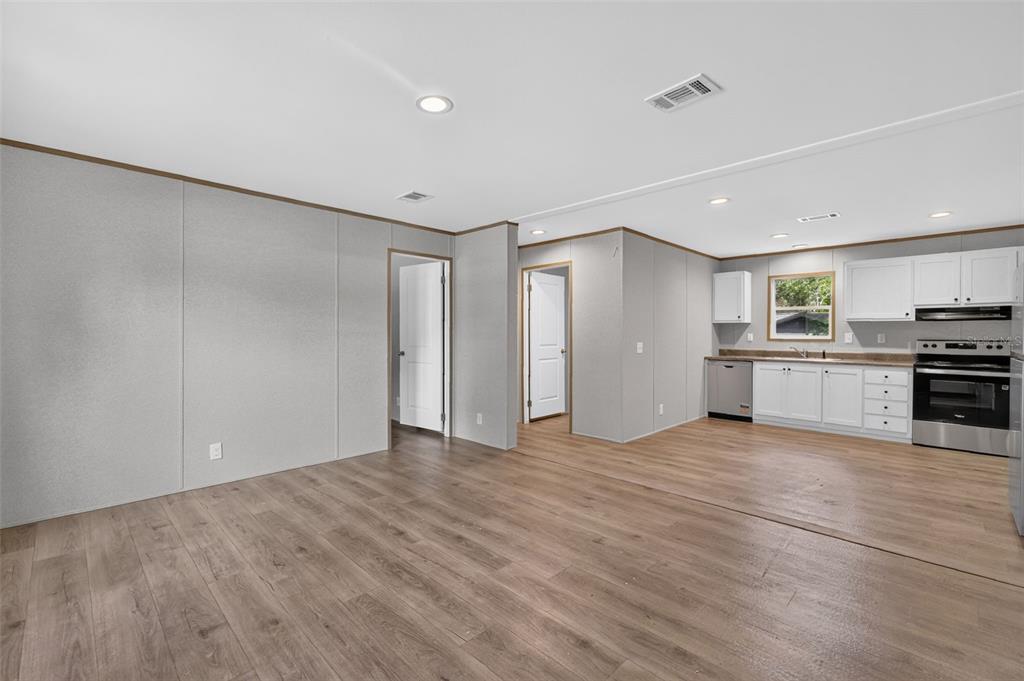 An open-concept living area with light gray walls, wood-look flooring, and a white kitchen — 607 LAWRENCE STREET, WILDWOOD, FL