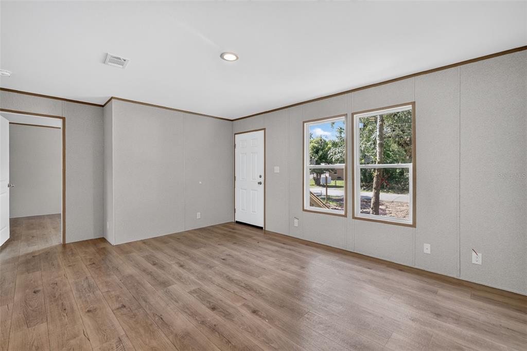 An empty room with gray paneled walls, wood-look flooring, a white door, and two windows — 607 LAWRENCE STREET, WILDWOOD, FL
