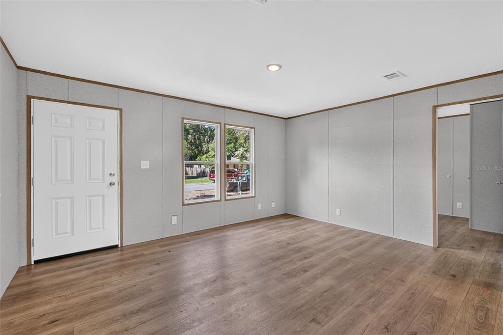 An empty room features light gray paneled walls, wood-look flooring, a white door, and windows — 607 LAWRENCE STREET, WILDWOOD, FL