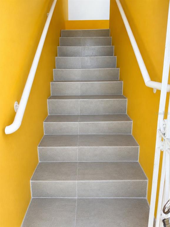 A staircase with gray tiled steps and white handrails between bright yellow walls — 54 CALLE DR. VEVE, BAYAMON, PR
