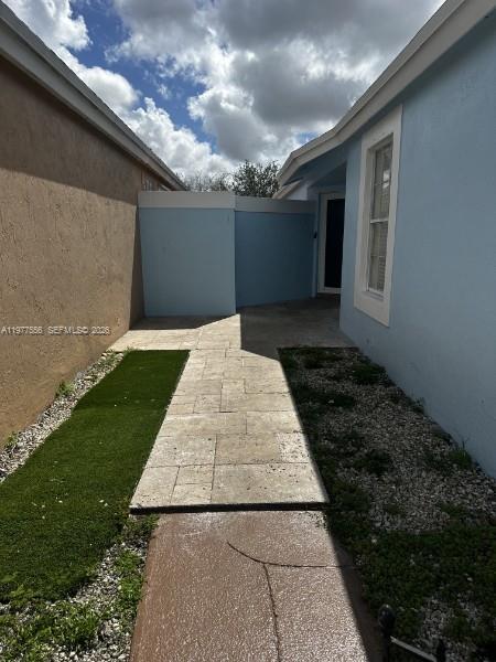 A paved walkway leads between a tan wall and a light blue house exterior — 14952 SW 75th Ter, Miami FL 33193, MIAMI, FL