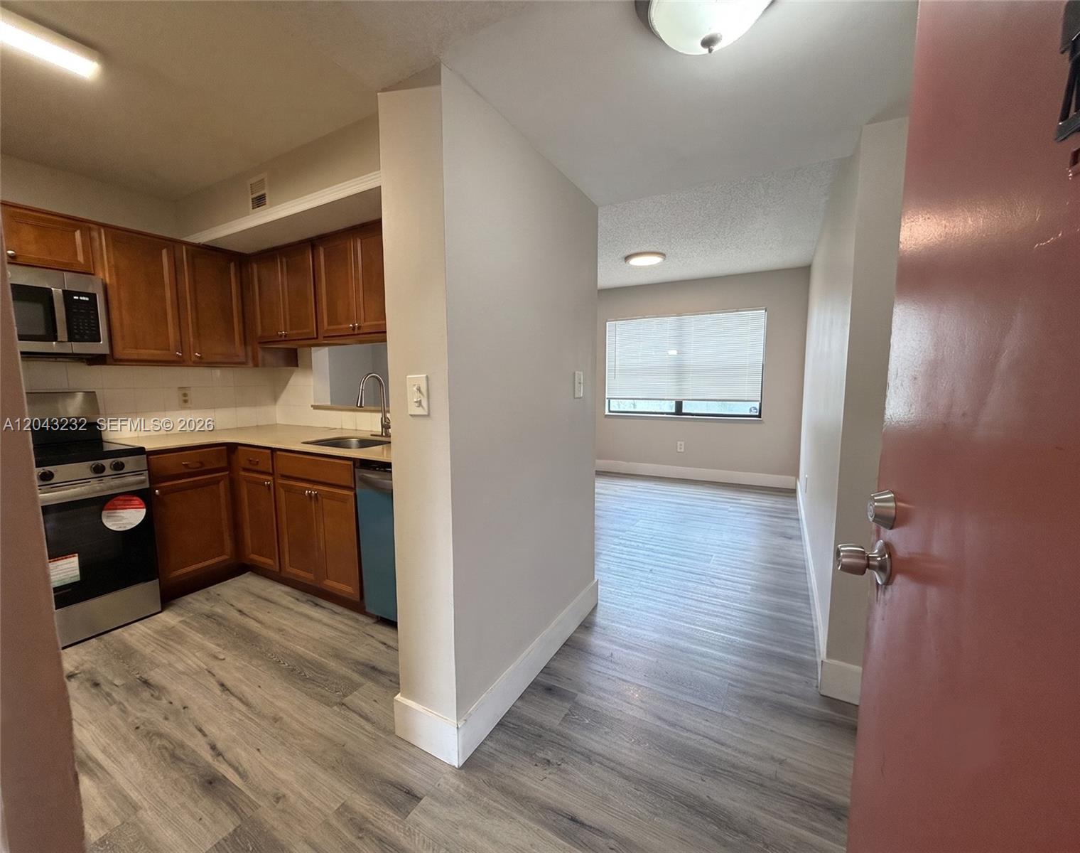 A kitchen with wood cabinets and stainless appliances opens into a living area with flooring — 3400 Foxcroft Rd # 215, Miramar FL 33025, MIRAMAR, FL